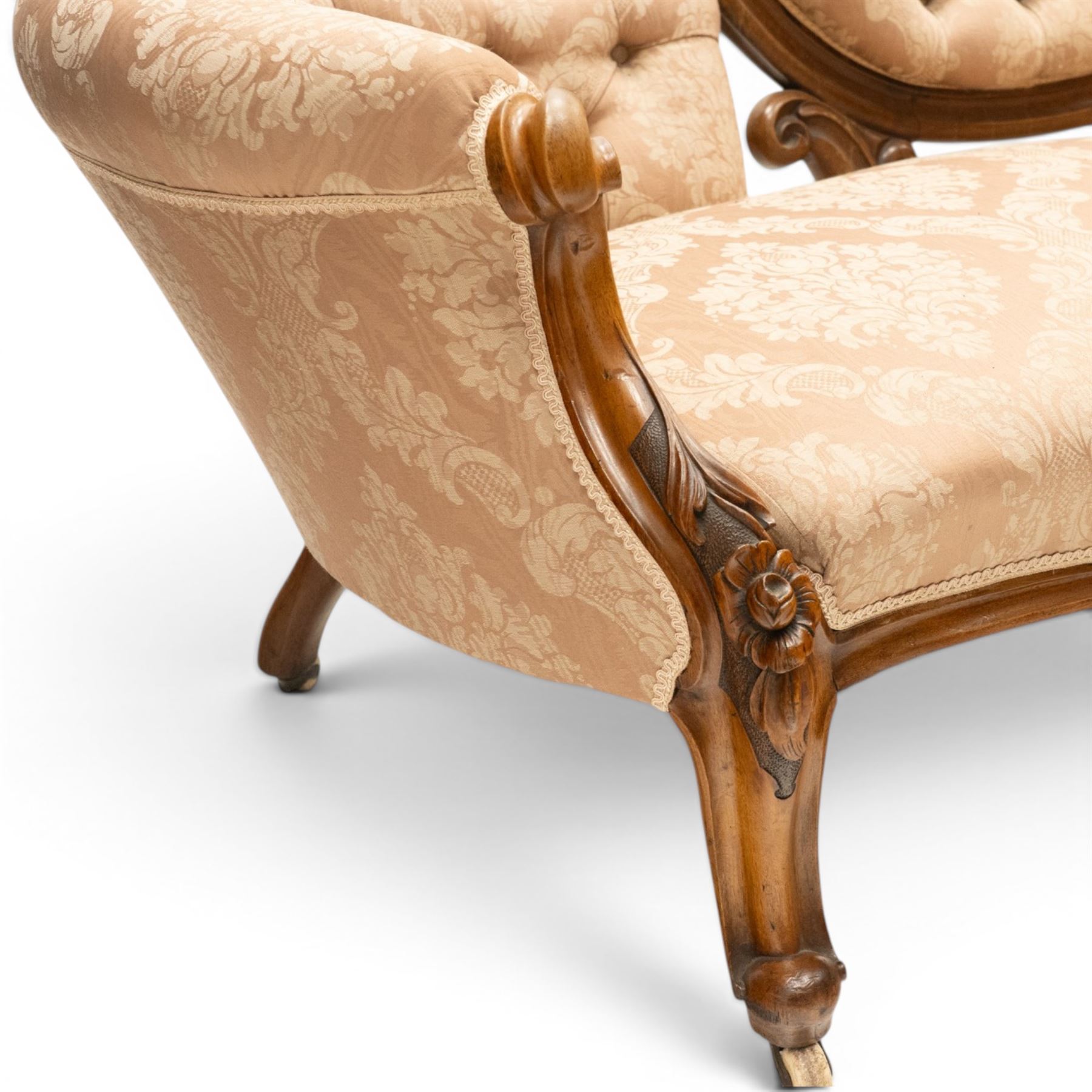 Victorian carved walnut framed double-ended settee with serpentine front, the central oval cameo back with flowerhead carved cresting rail, flanked by foliate C-scroll spandrels, the scroll carved arm terminals over floral carved cabriole supports with scroll feet and ceramic castors, the buttoned back and sprung seat upholstered in pale pink foliate patterned damask fabric