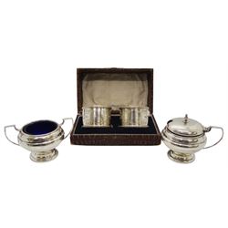 Pair of early 20th century silver cruets, comprising twin handled open salt, and mustard pot and cover, each of squat circular form upon a circular stepped base, with blue glass liners, hallmarked Walker & Hall, Sheffield 1919, together with a pair of 1920's silver napkin rings, each with foliate engraved decoration, hallmarked Robert Pringle & Sons, London 1927, contained within a fitted case, approximate total silver weight 5.86 ozt (182.3 grams)