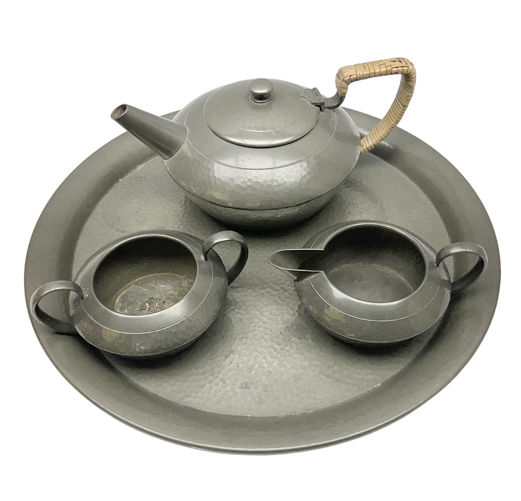 Liberty & Co Tudric pewter three piece tea service, comprising teapot with woven reed handle, twin handled open sucrier, and milk jug, each of squat form with planished finish, each impressed beneath Tudric Pewter Ware 01537 Made in England, together with a matched unmarked tray