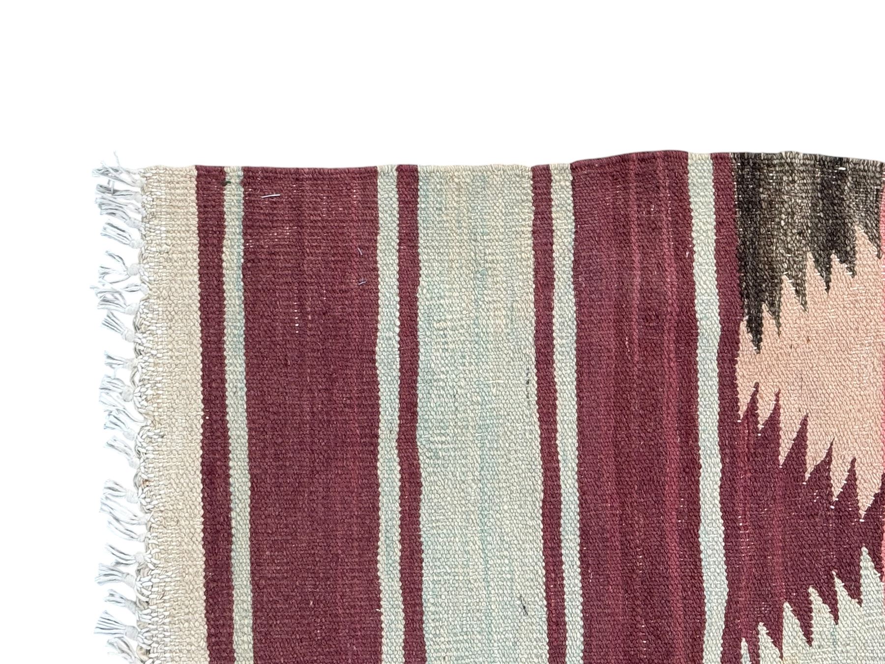 Kilim muted pink ground runner, decorated with rows of horizontal bands in muted tones, alternating with geometric triangular patterns along each band, fringed ends