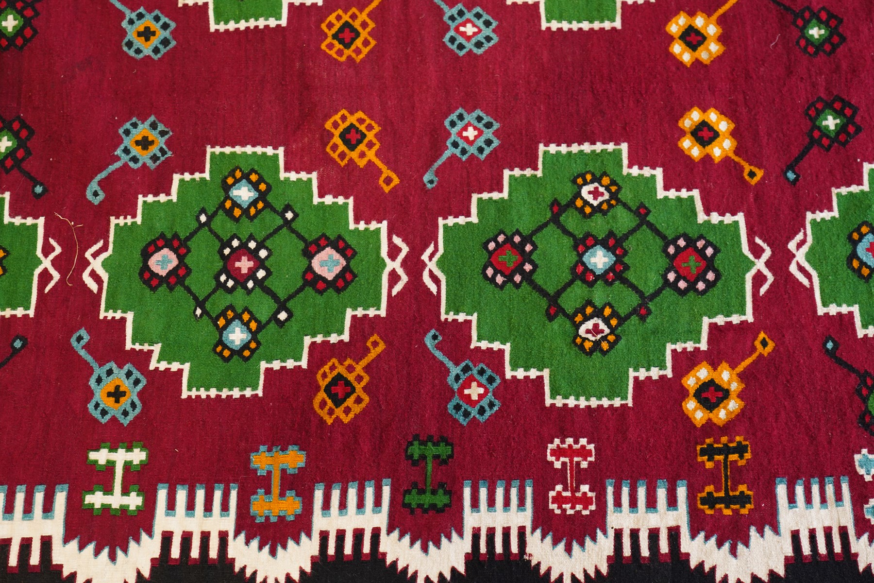 Persian Fars province crimson ground kilim rug, decorated with two rows of geometric emerald green motifs containing stylised plant designs, enclosed by an ivory and dark indigo guard band