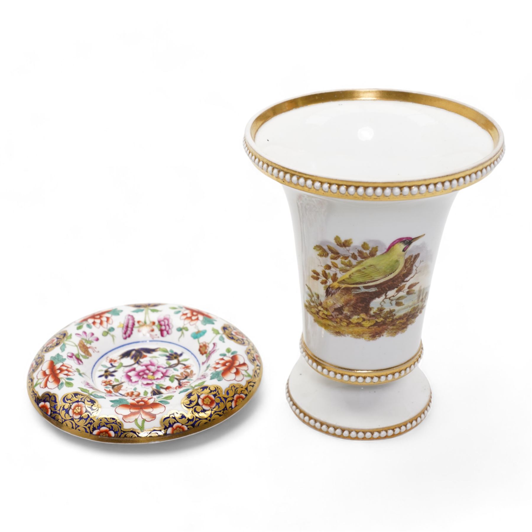 Early 19th century Spode spill vase, of cylindrical form with flared rim, hand painted with a Green Woodpecker perched on a branch, within beaded borders, titled beneath, H16cm, together with a Spode chocolate cup turnover rim stand, decorated in the imari pattern, no. 2630, painted marks beneath, D14cm (2)
