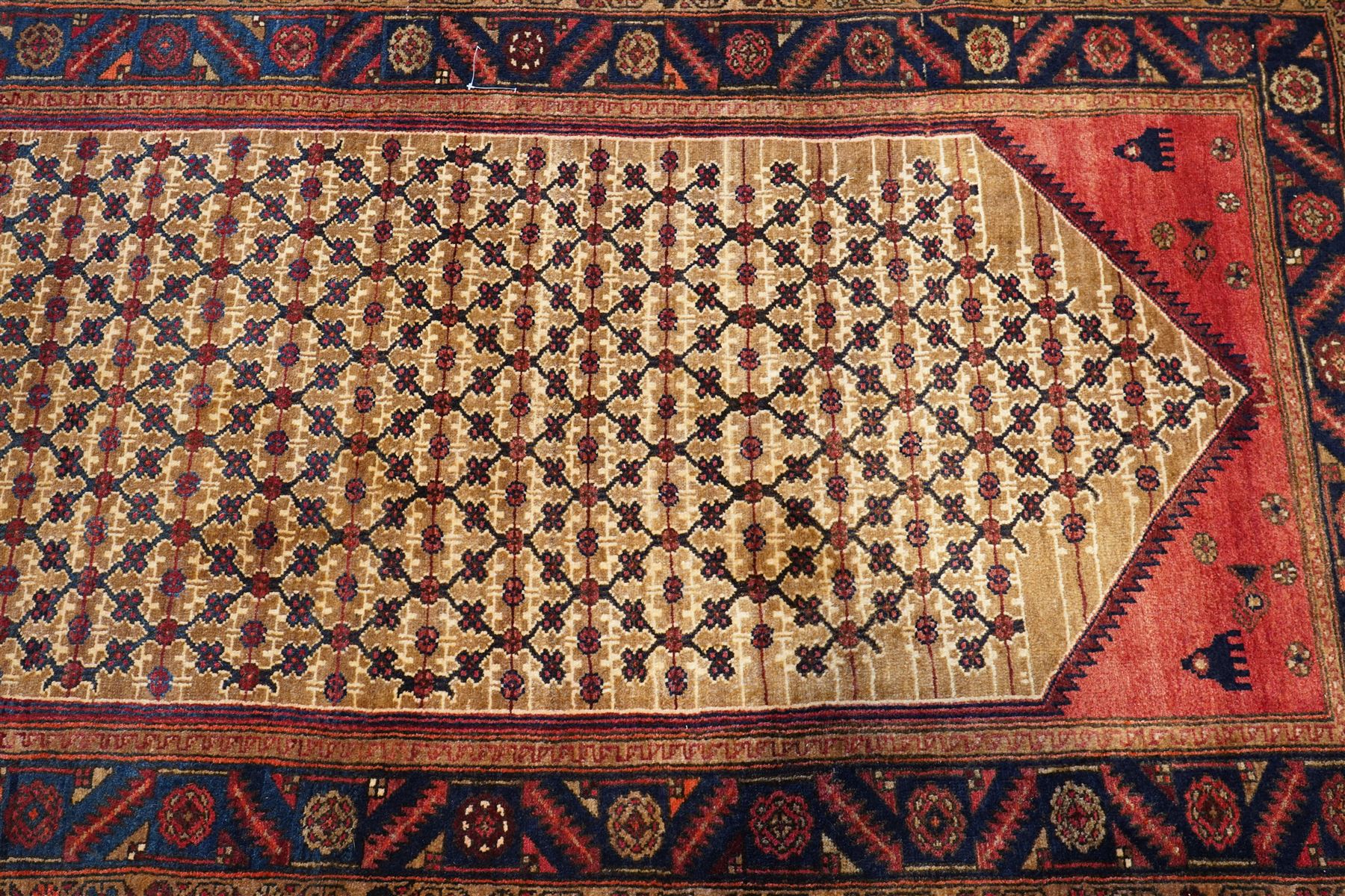 North East Persian Kurdie hand-knotted runner, camel ground with an all-over lattice of rosette motifs linked by angular vines, terminating in a stepped lozenge panel, with a madder red field, spandrels with geometric and zoomorphic devices, indigo main border of angular vines and repeating rosettes, flanked by narrow guard stripes, cotton fringe ends  