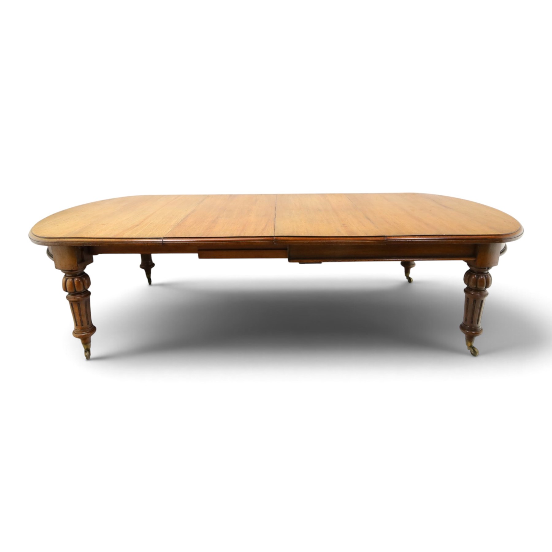 Large Victorian oak extending dining table, the rectangular top with rounded corners and moulded edge, plain frieze over large turned lobed and fluted supports terminating to brass cups and castors, with two additional leaves