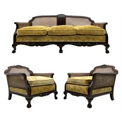 Early 20th century mahogany three piece bergère suite, three seat settee and pair matching armchairs, the moulded cresting rails with carved scrolled acanthus leaves and pierced lattice decoration, acanthus carved scrolled arm terminals and shaped lower rail, on hairy paw carved feet, upholstered in gold fabric with floral pattern, loose feather cushions, double caned sides