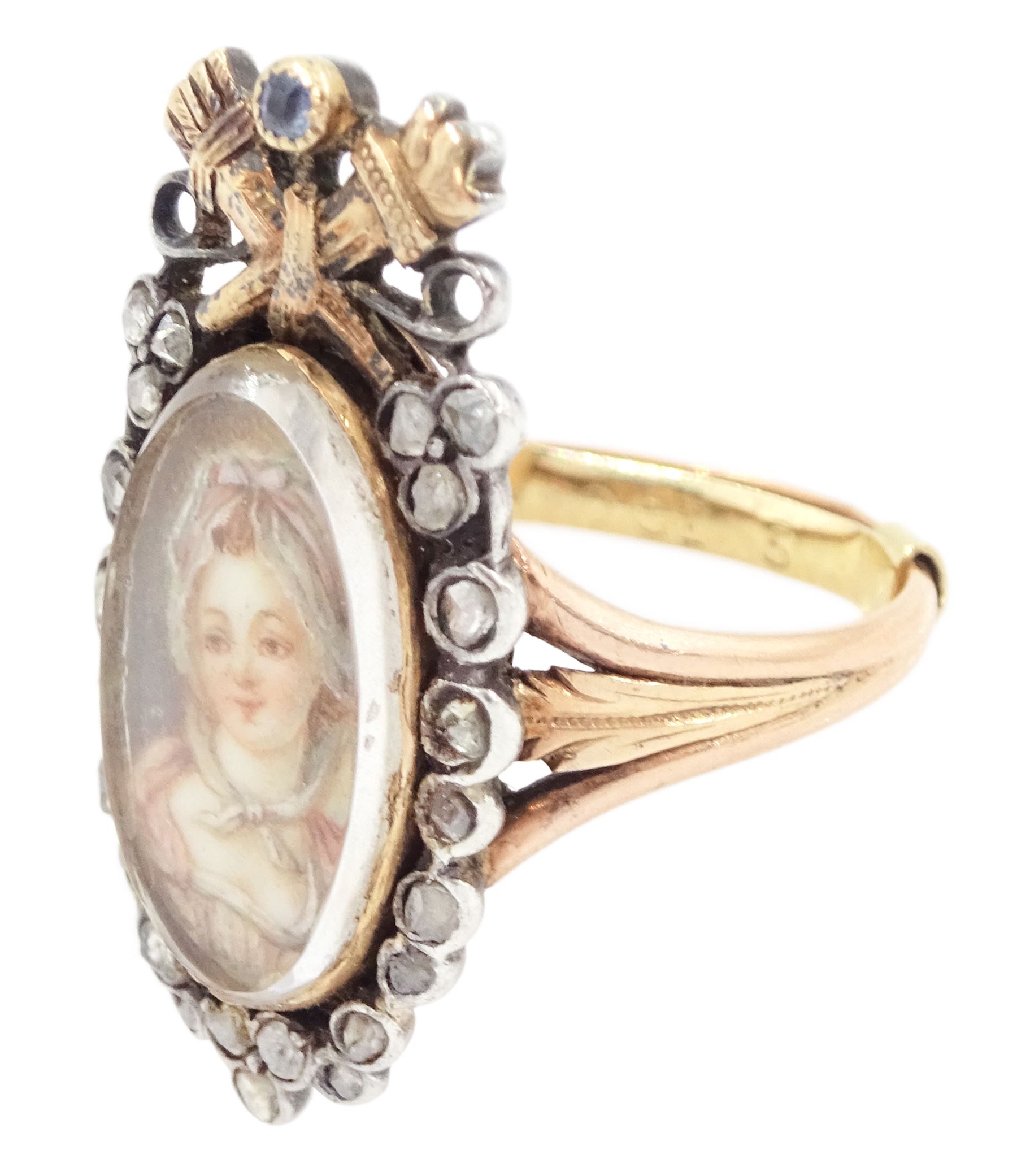 18th / 19th century silver and gold diamond and sapphire portrait ring, set with an oval miniature of a woman wearing a bonnet on ivory, under a glazed panel, surmounted with a 'trophy of love' symbol, modelled as a flaming torch and bow and quiver, set with a single round cut sapphire and rose cut diamond surround, to trifurcated shoulders, on French 18ct gold shank, Eagle hallmark. This lot has been registered for sale under Section 10 of the APHA Ivory Act