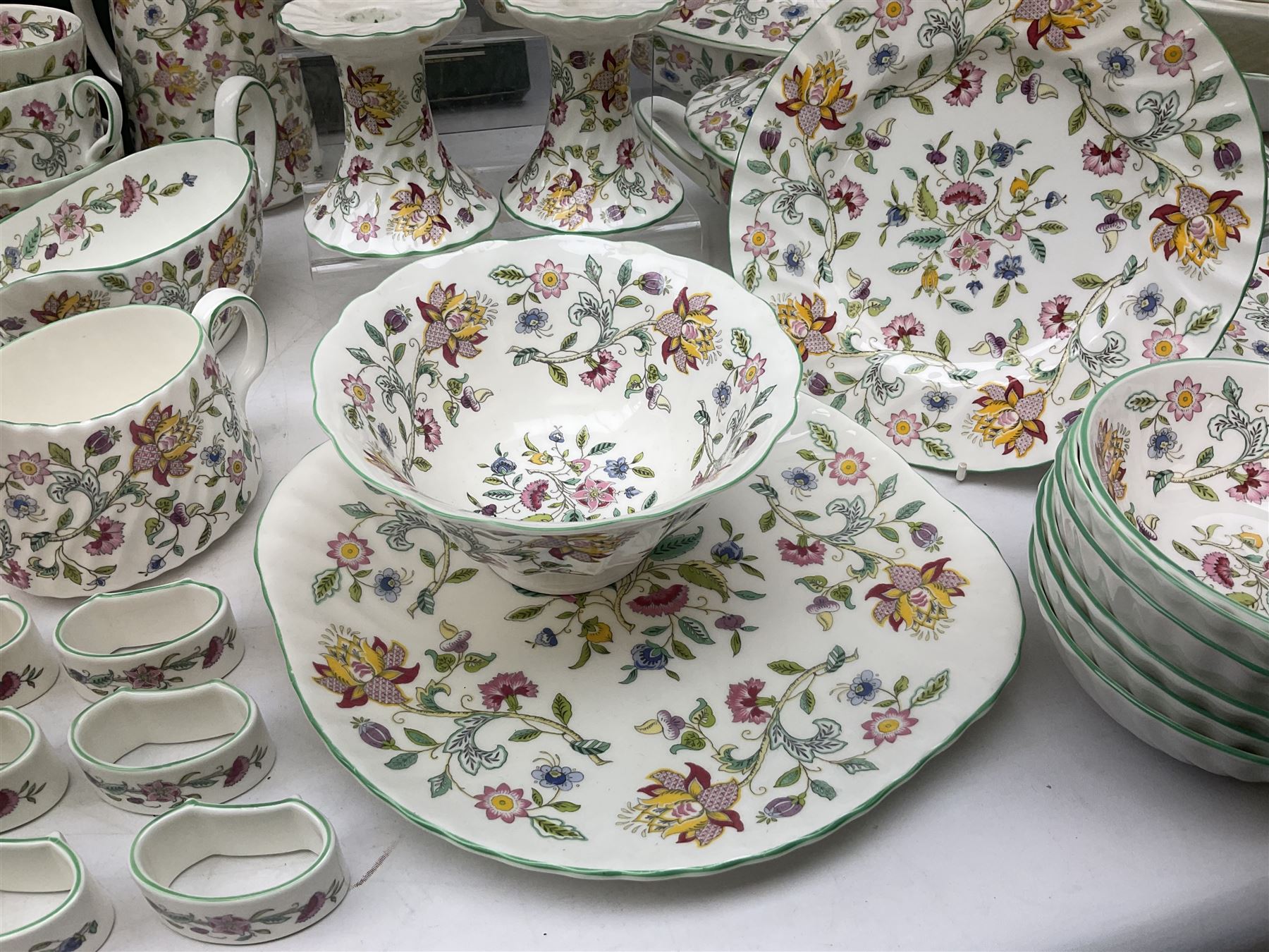 Minton Haddon Hall pattern tea and dinner wares, including basket dish, two covered tureens, six dinner plates, eight dessert plates, twelve tea plates, six soup bowls, six cereal bowls, teapot, coffee pot, milk jug, covered sucrier twelve tea cups and saucers, six mugs, footed bon bon dish, pair of candlestick holders, cake knife and slice etc (81)