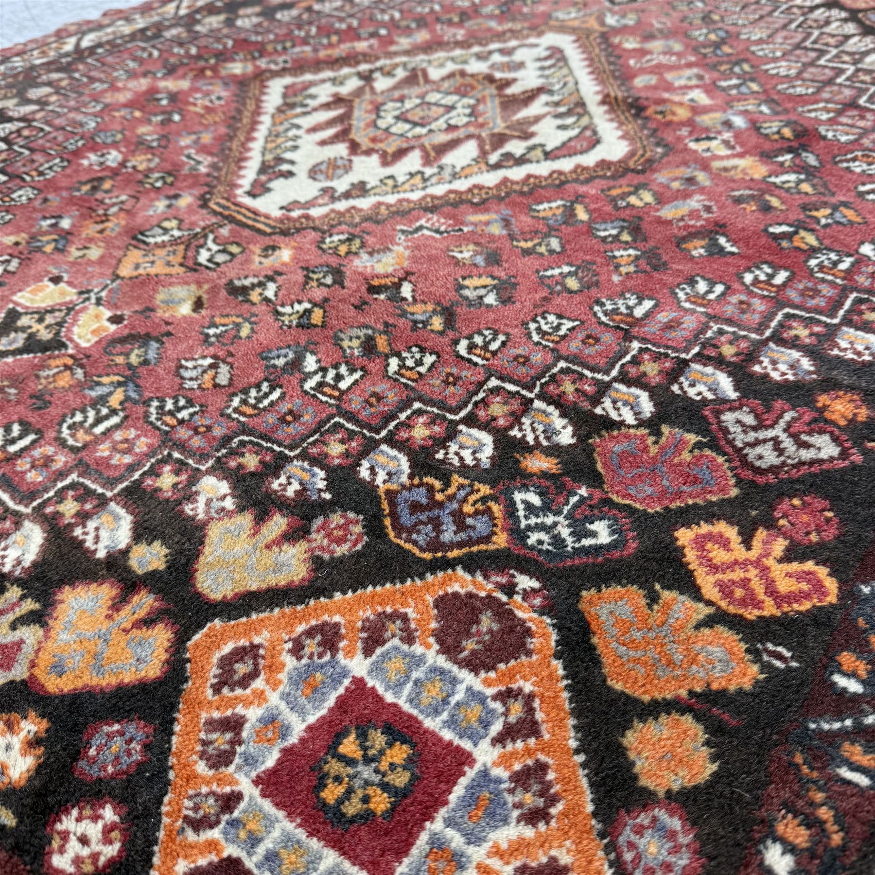 Southwestern Persian Qashqai rug, central diamond medallion with hooked motifs flanked by four corner medallions on a rich red madder field with dark brown ground of stylized floral and animal motifs, and ivory border with alternating floral palmettes and a red main  border with a meandering vine pattern 