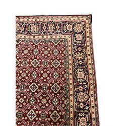 Persian red ground rug, the field decorated with repeating floral pattern, scrolling border with stylised plant motifs