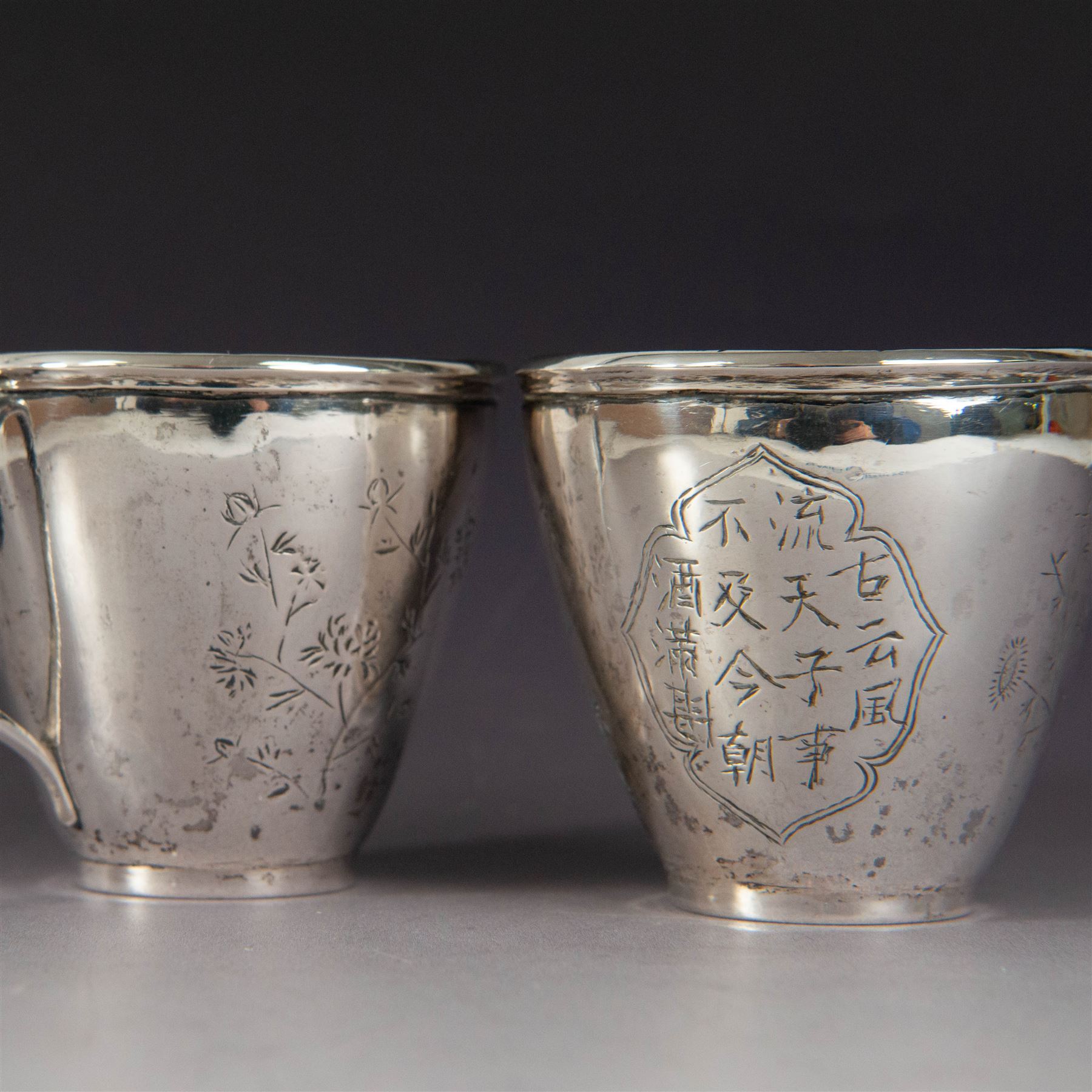Pair of Chinese export silver teacups, both decorated with character marks, one with floral decoration, the other decorated with a bird within bamboo branches, both with indistinct maker's marks beneath, H6cm
