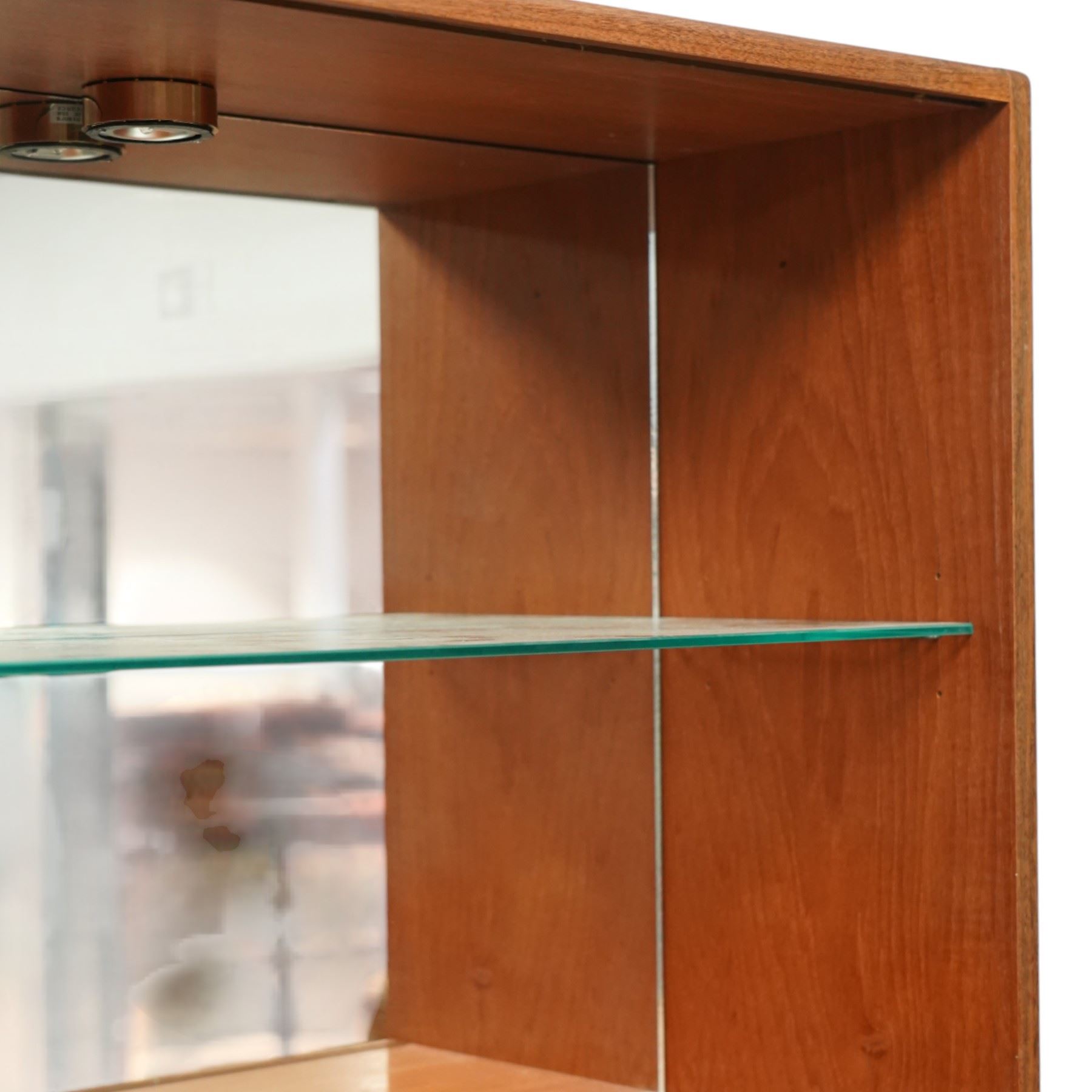 G-Plan - ‘Fresco’ teak bookcase cabinet, rectangular open bookcase with mirrored back panel to the upper section, fitted with a single glass display shelf and two wooden shelves below, the base enclosed by a pair of cupboard doors with shaped teak handles, on a plinth base