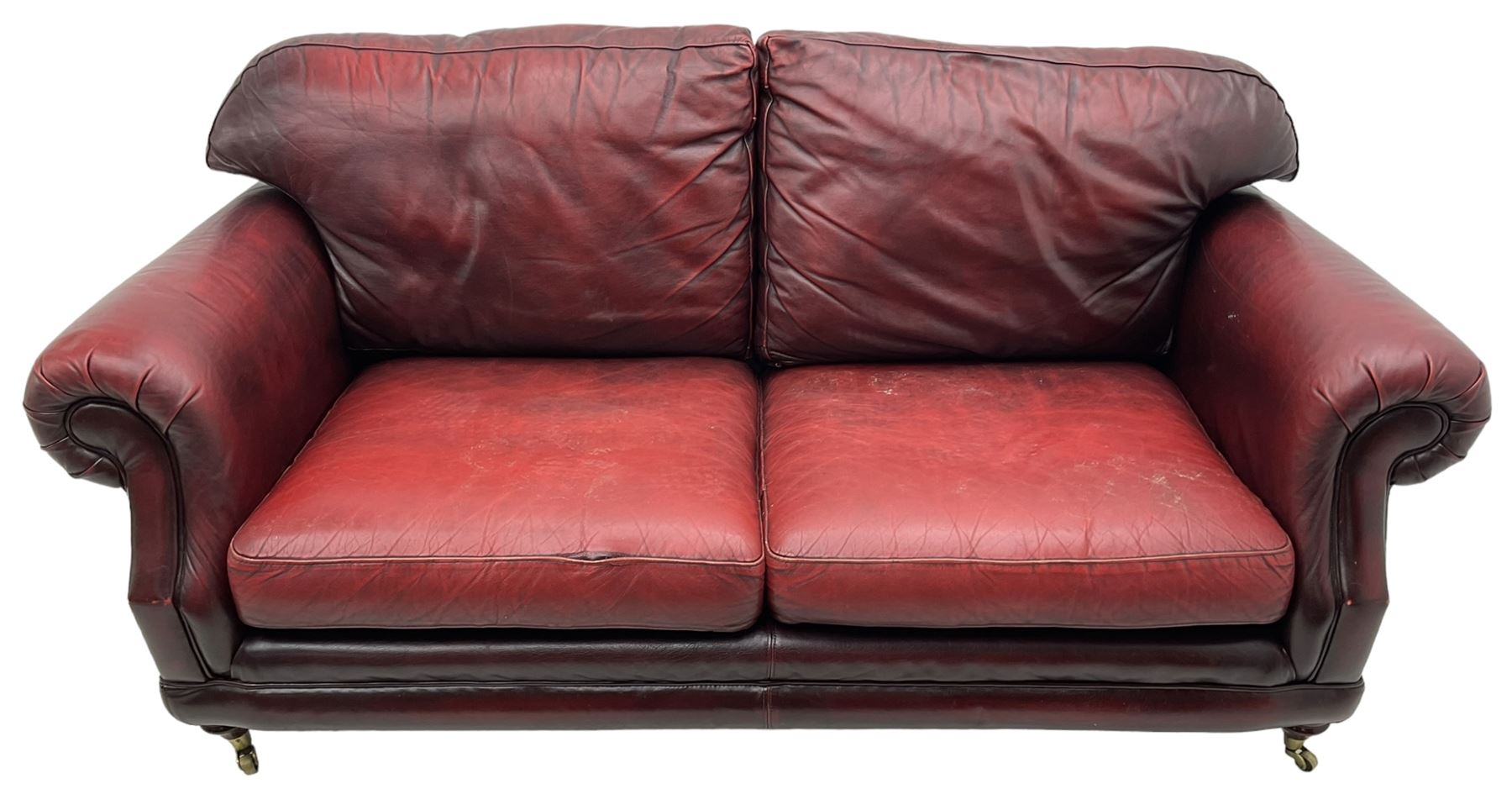 Thomas Lloyd - three-piece lounge suite, comprising of traditional shape two seat sofa (W190cm H80cm) and a pair of wingback armchairs (W100cm H91cm), each with rolled arms over turned supports with brass castors, upholstered in oxblood red leather