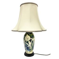Moorcroft table lamp of baluster form, decorated with white flowers amongst foliage on merging dark blue and cream ground, raised upon circular spreading base, with original label and gilt stamp to the felt lined base, H29cm excl fitting