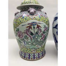 Chinese jar and cover, decorated in polychrome enamels with a panel depicting birds amongst peonies, surrounded by floral and foliate decoration on a yellow ground, with four pink mask handles and dog finial to cover, with retail sticker beneath for Wing Tung Hing, together with a similar blue and white example, decorated with figural scenes amongst trees and flowers, the cover with a temple dog finial, with printed mark beneath, tallest H41cm