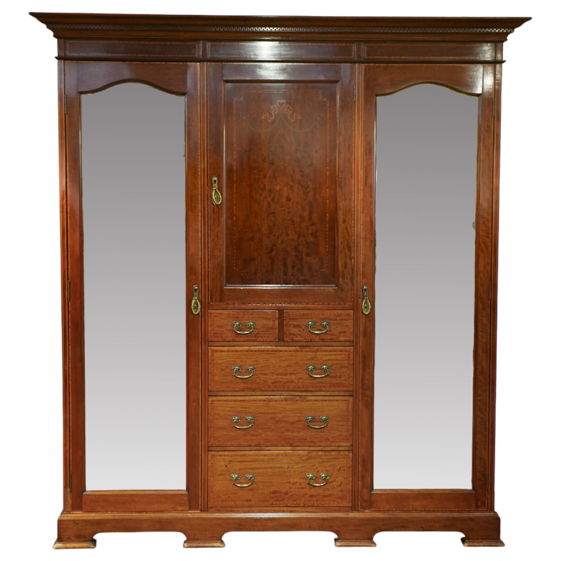 Edwardian mahogany triple combination wardrobe, the moulded cornice above a central panel door inlaid with foliate detail, flanked by full length mirrored doors, the interior fitted with hanging compartments and a central bank of two short and three long drawers, raised on a shaped bracket feet