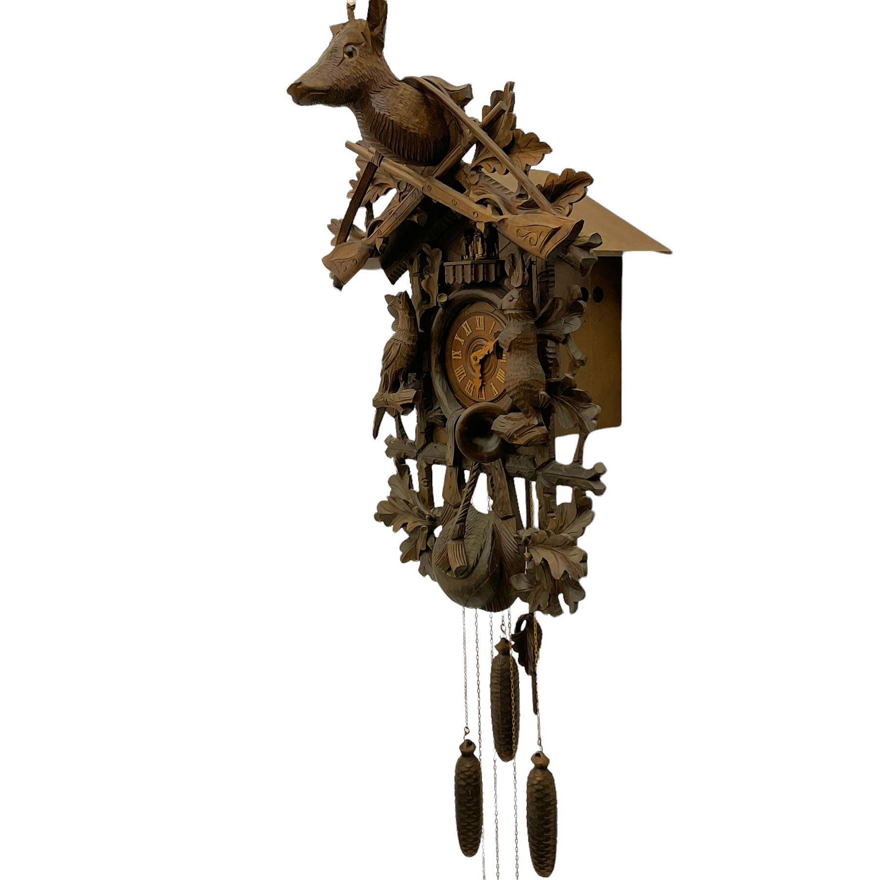 A large and imposing 20th century three train 30hr cuckoo clock with automata and musical features, profusely carved case with a carousel, animals, leaves and sporting guns, dial with pierced wooden numerals and wooden hands, with three weights and pendulum, strike/silent facility. 
