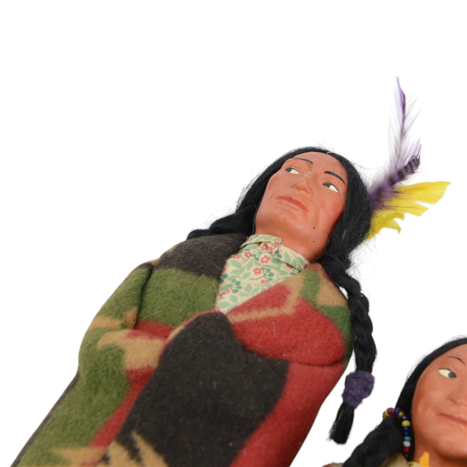 Two Skookum Native American Indian dolls with foot label, with painted composition heads, side glancing eyes, black hair wig, stuffed rigid body, original clothes, the male with feather headdress, the female with baby on back, H32cm