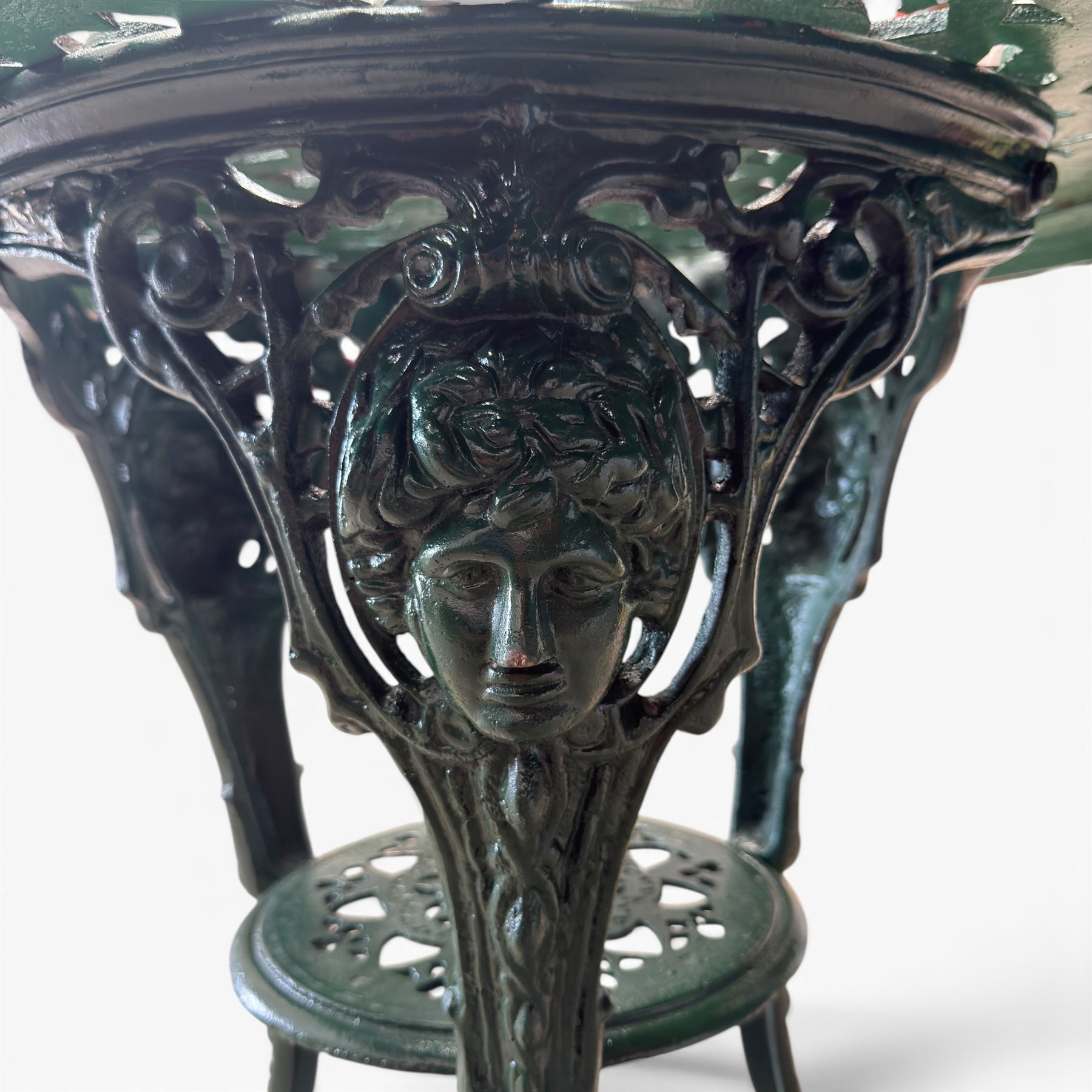 Painted cast iron garden table, the circular pierced top with foliate decoration and egg-and-dart rim, raised on three cloven hoof supports with classical female mask knees, united by pierced undertier, in green-painted finish