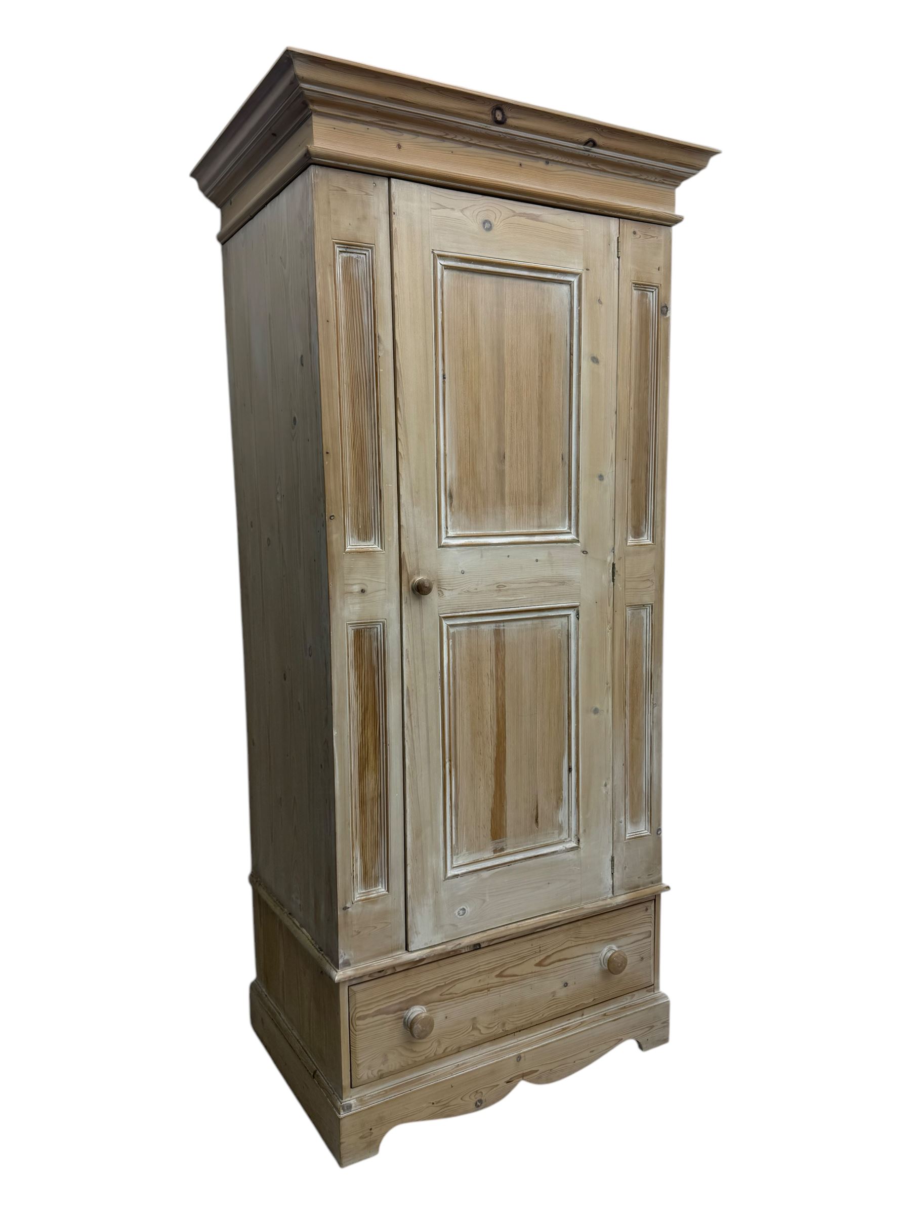 Victorian design lime-washed pine single wardrobe, projecting cornice over panelled door enclosing hanging rail, the lower section fitted with full-width drawer, on shaped plinth base