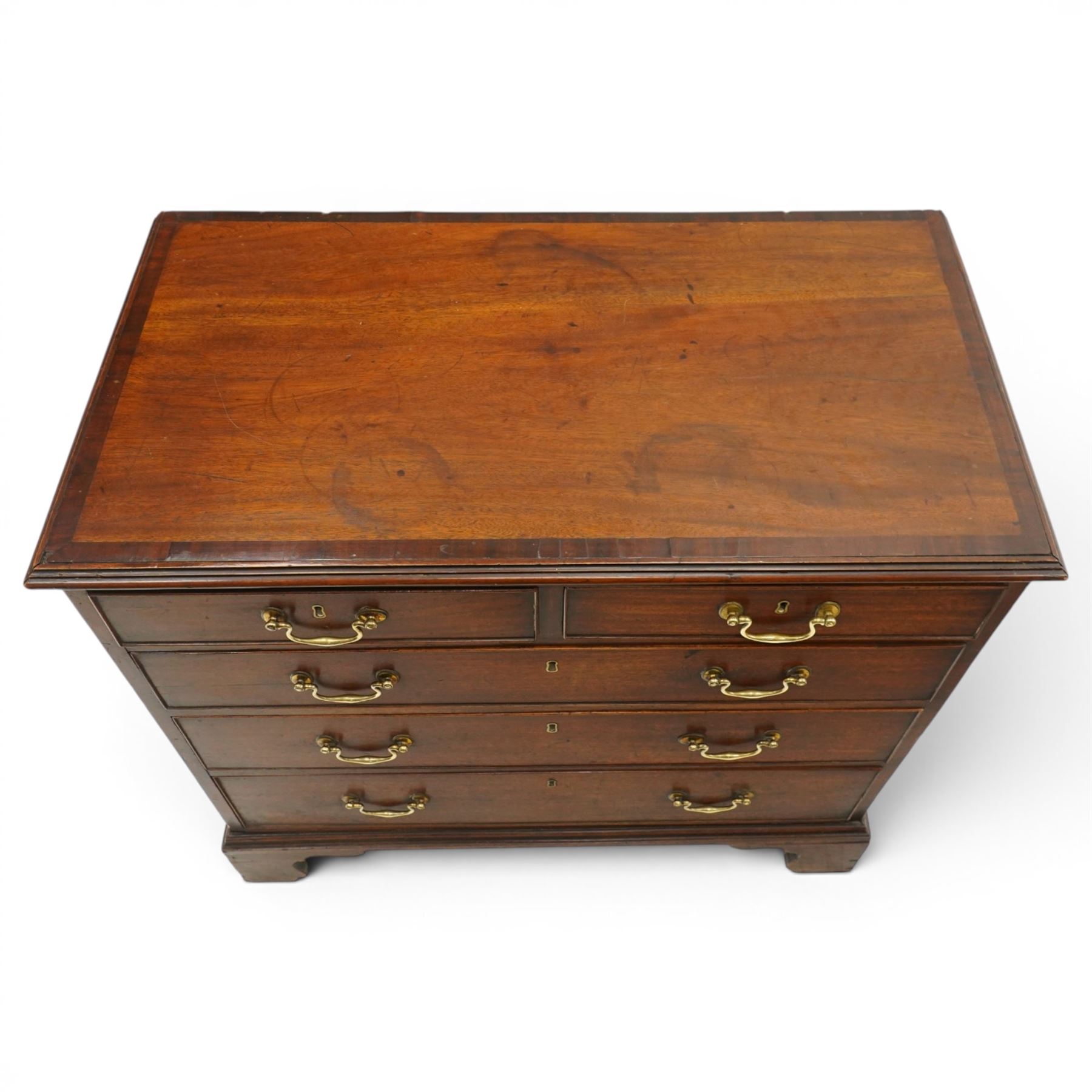 Late 18th century mahogany chest of drawers, rectangular top with moulded edge above two short and three long graduated drawers, with brass swan neck handles, shaped apron and bracket feet