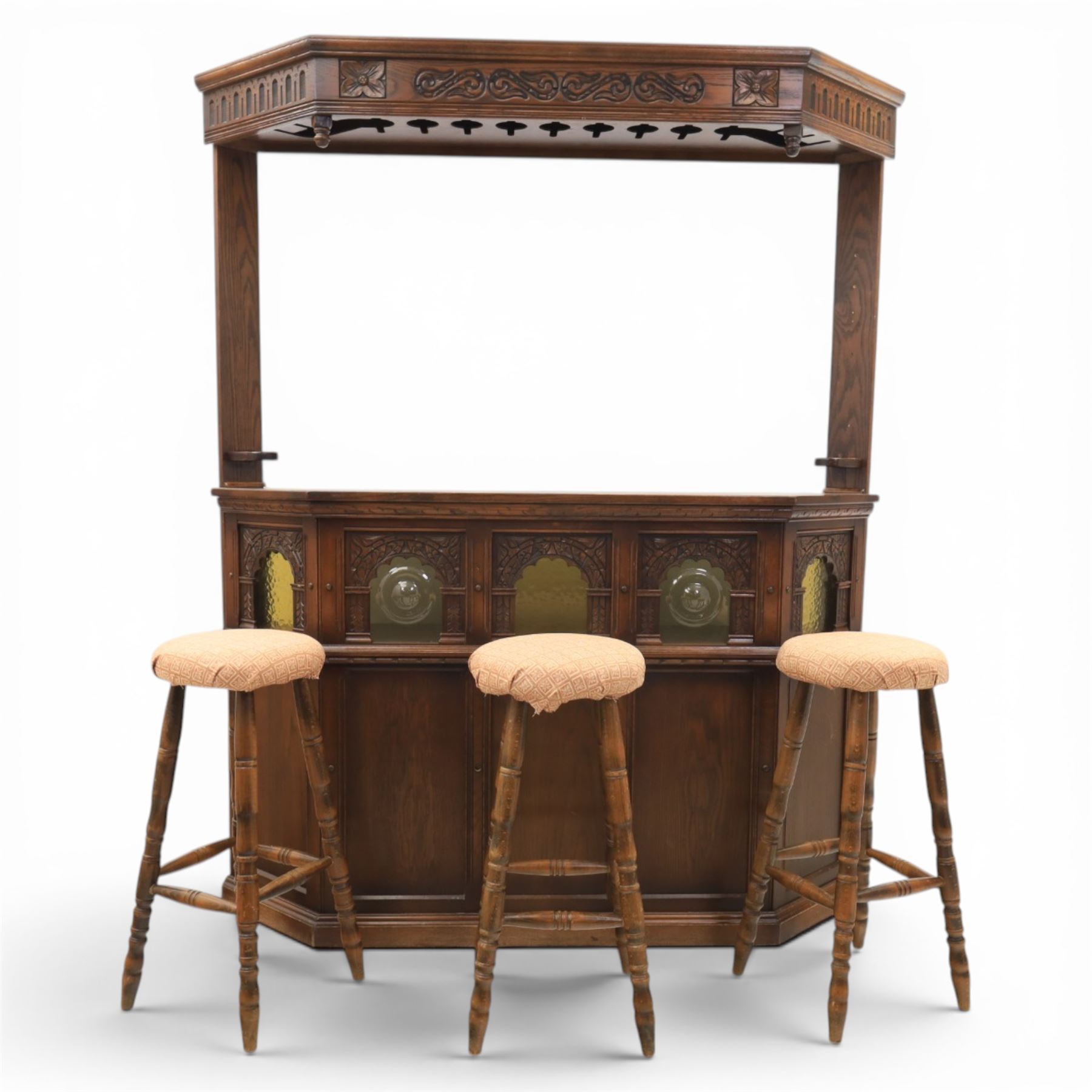 Old Charm - carved oak bar with three bar stools and associated Old Charm drinks cabinet, carved top with channels for glassware beneath, bar surface above glazed panels, shelves for glassware to the back, associated Old Charm drinks cabinet with fall front linenfold carving, above twin doors with shelved interior
