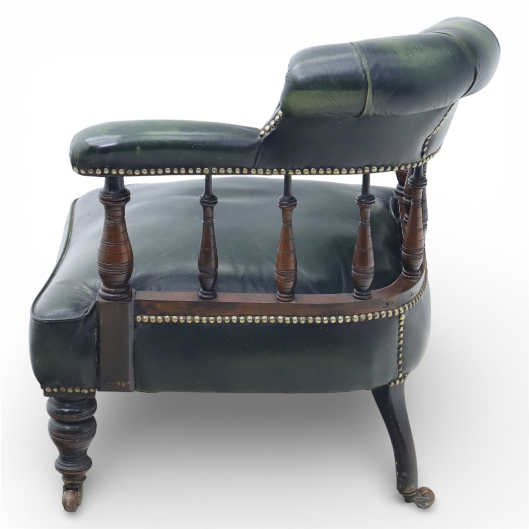 19th century green leather upholstered corner chair, with deep buttoned back and swept padded arms with close studded borders, raised on turned supports united by turned spindles, terminating in brass castors