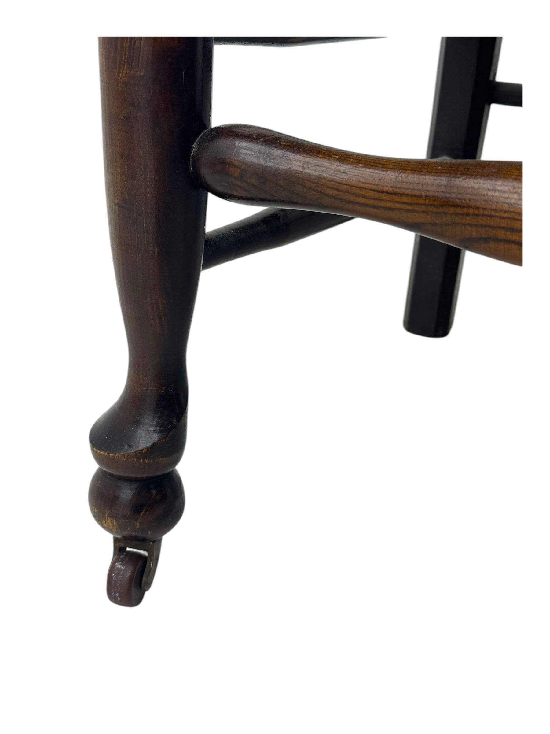 Early 19th century ash armchair, the back with winged spindles extending from a shaped top rail, above a splat of two rows of vertical spindles, with curved arms and a rush seat, raised on turned supports united by double stretchers terminating in castors