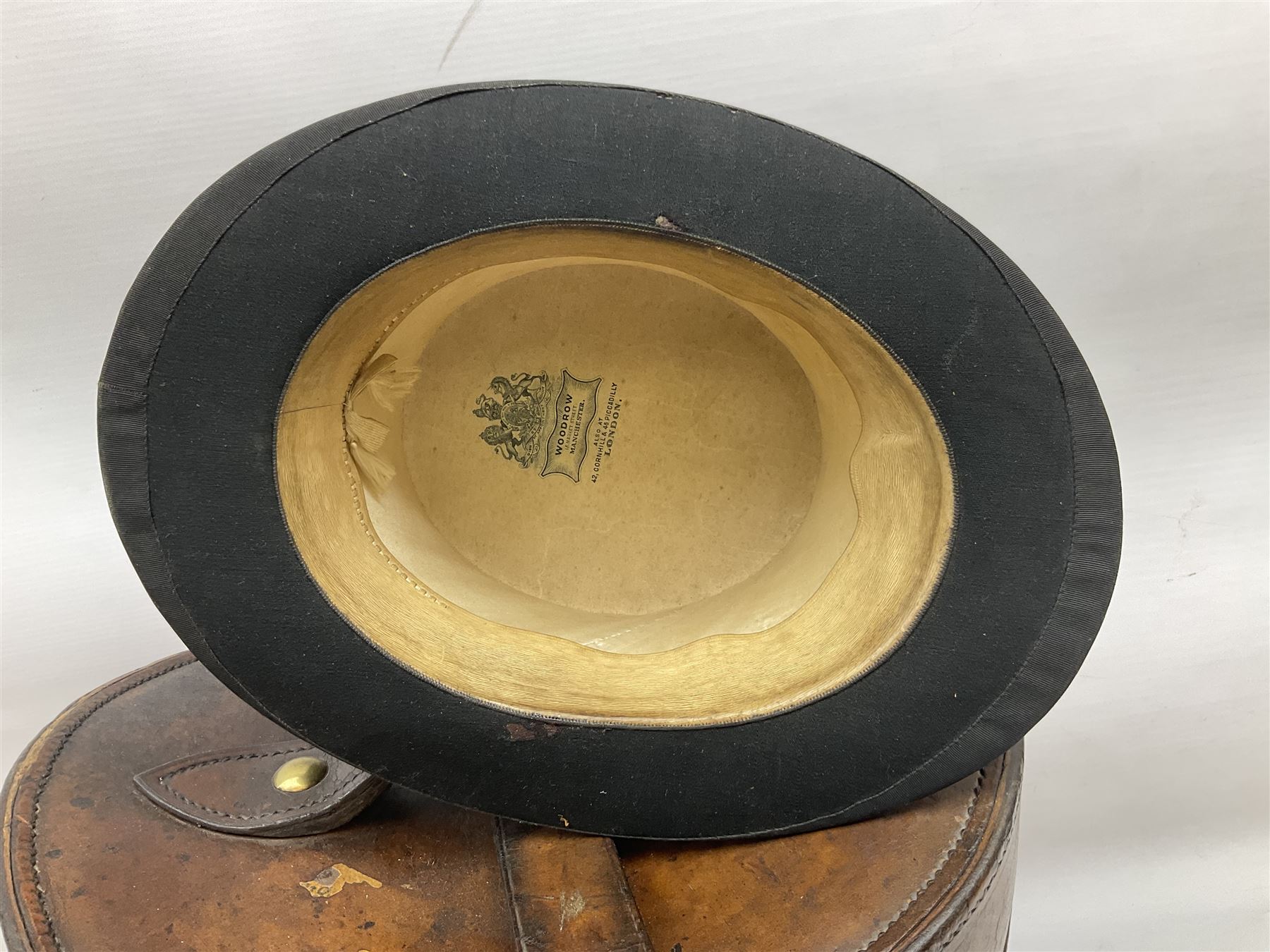 Early 20th century black silk top hat by Woodrow of Manchester and London, with manufacturer's stamp to the silk lined interior, housed in fitted tan leather hat box with removable internal compartments with straps, brass escutcheon and engraved plaque, hat internal measurements approx 20cm x 15cm