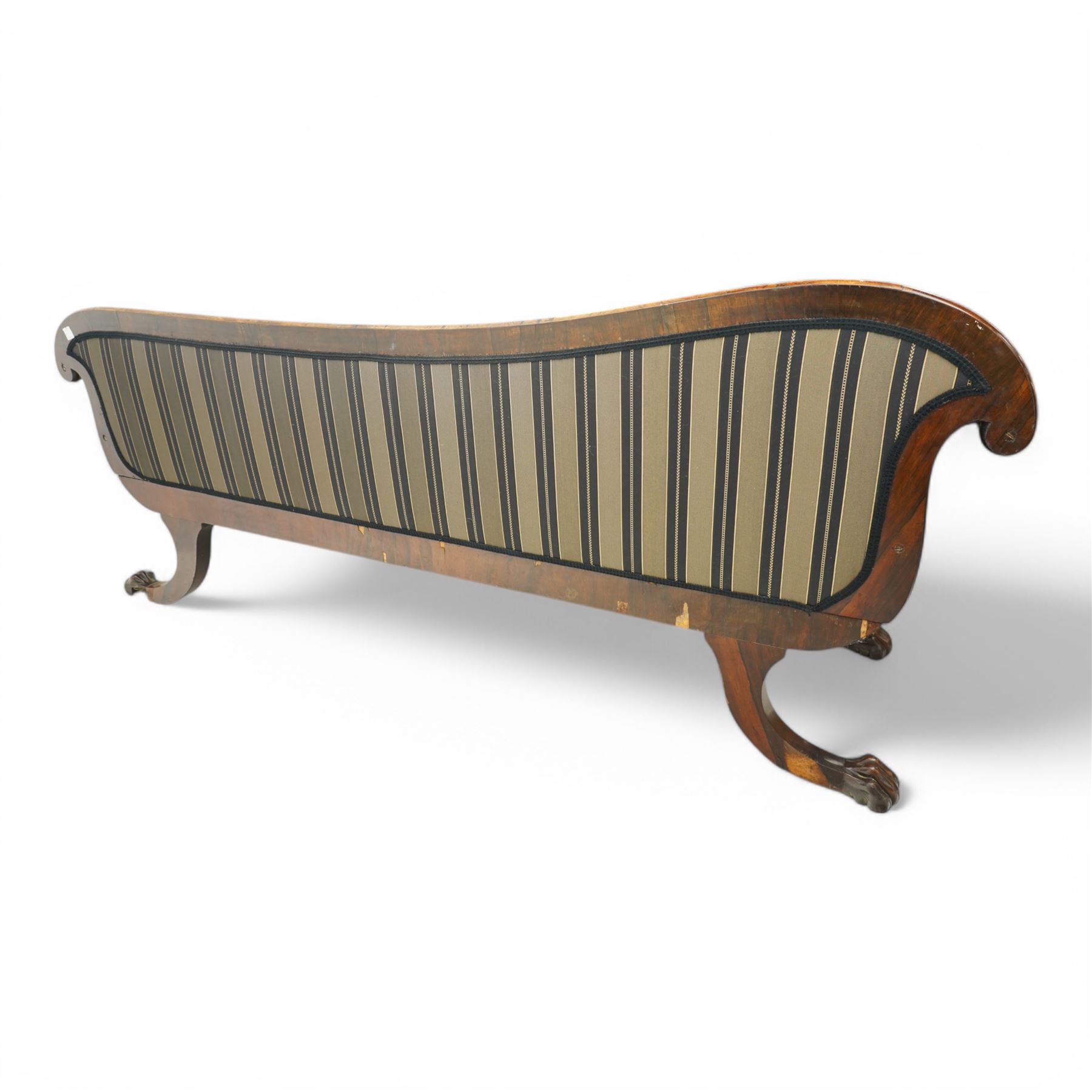 Regency brass inlaid rosewood chaise lounge or settee, shaped back over rolled head and foot, upholstered in black and gold striped fabric with rectangular squab cushion and bolster cushion, the rolled terminals carved with acanthus leaf roundels, lower rectangular foliate carved panels, on out splayed supports with paw carved feet 