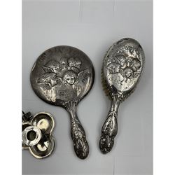Victorian silver chamber stick, in the form of a shamrock with heart loop handle, hallmarked Stokes & Ireland Ltd, Birmingham 1892, Edwardian silver mounted handheld mirror, decorated in relief with a group of cherubs, with engraved initials, hallmarked Birmingham 1907, maker's mark indistinct and a similar silver mounted hairbrush, hallmarked Henry Matthews, Birmingham 1907, approximate weighable silver 1.67 ozt (51.8 grams)