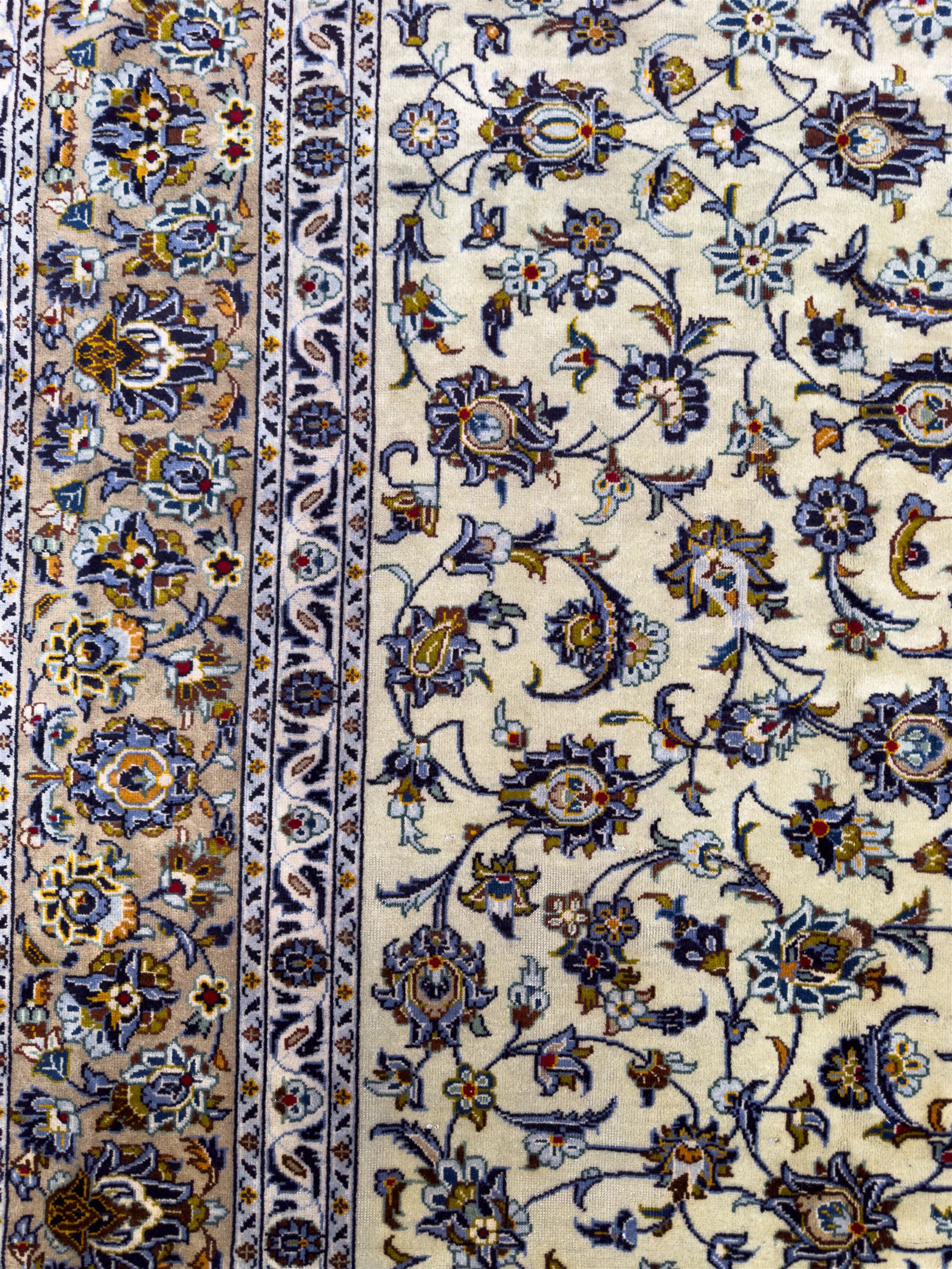 Central Persian Kashan hand-knotted carpet, ivory field with an all-over design of scrolling vines, lotus palmettes, and rosettes in shades of blue, gold, and brown within a blue ground border of palmettes and arabesques between multiple guard stripes