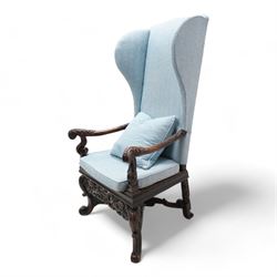 Carolean design walnut and oak wingback open armchair, the high wingback upholstered in light blue herringbone fabric, acanthus leaf carved arms with scrolled terminals and on scrolled supports, cane work seat with squab cushion and scatter cushion, the lower rail carved and pierced with putti holding crown surrounded by curled acanthus leaves, leaf carved S-scroll supports united by Scrolled X-framed stretchers 
