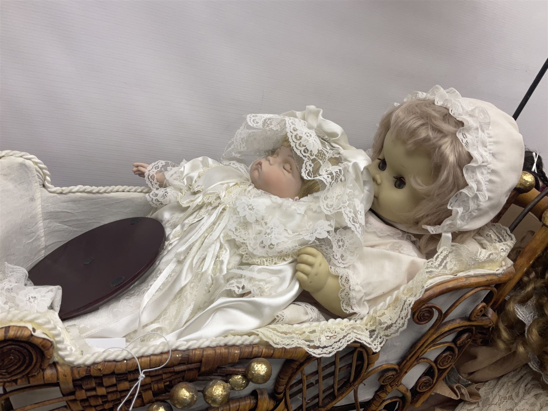 Two decorative wicker dolls prams, one with lace parasol,  and eleven dolls, including Leonardo Collection porcelain dolls, tallest pram including parasol H105cm