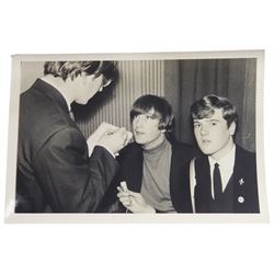 John Lennon interview recording conducted by John Hill student of Hull University on the 16th October 1964 at the A.B.C. Theatre Hull on behalf of the university newspaper 'Torchlight'. The interview lasts eight and a half minutes. It catches John in an upbeat breezy mood answering questions about the following topics: the song writing process ('sometimes you get an idea ....I dunno....my left leg.... and then write about that....'), recording (.... 'they just say - you're recording on such and such a date and they hope we turn up with some good songs written ....'), an alternative career path (.... 'I'd probably just have been a lay-about....'), failing at college (....'some other lads did my exams for me ....'), reading matter ( Clockwork Orange, Alice in Wonderland), his books of prose, tastes in music, the Blues, The Rolling Stones, being a Beatle vis-a-vis anonymity ('Whatever I'd be I'd choose to be rich .... who wants to walk down the street?').
The interview was recorded on 1/4 inch Emitape on a Fi-Cord Fidelity Recording machine. The reel-to-reel tape comes in its original Emitape plastic box and is accompanied by the Fi-Cord reel-to-reel machine on which the interview was originally recorded. Also included in this lot are a copy of the 'Torchlight' newspaper from 21st November 1964, two photographs of the interviewer with John Lennon (the interviewer is pictured to the left of John Lennon in the photograph in which John is signing a sketch) and one photograph of Paul McCartney with another reporter, the largest measures 12 x 16.5cm and a transcript of the interview. The recording is also accompanied by the original Fi-Cord tape recorder with microphone, four original 2v batteries and battery charger. The tape recorder has been adapted to take 3xAA batteries and the 2v battery charger is fitted with a standard UK 3-pin AC plug. The interview was recorded in the press room prior to the Beatles concert at the A.B.C. Theatre and is sold with copyright.