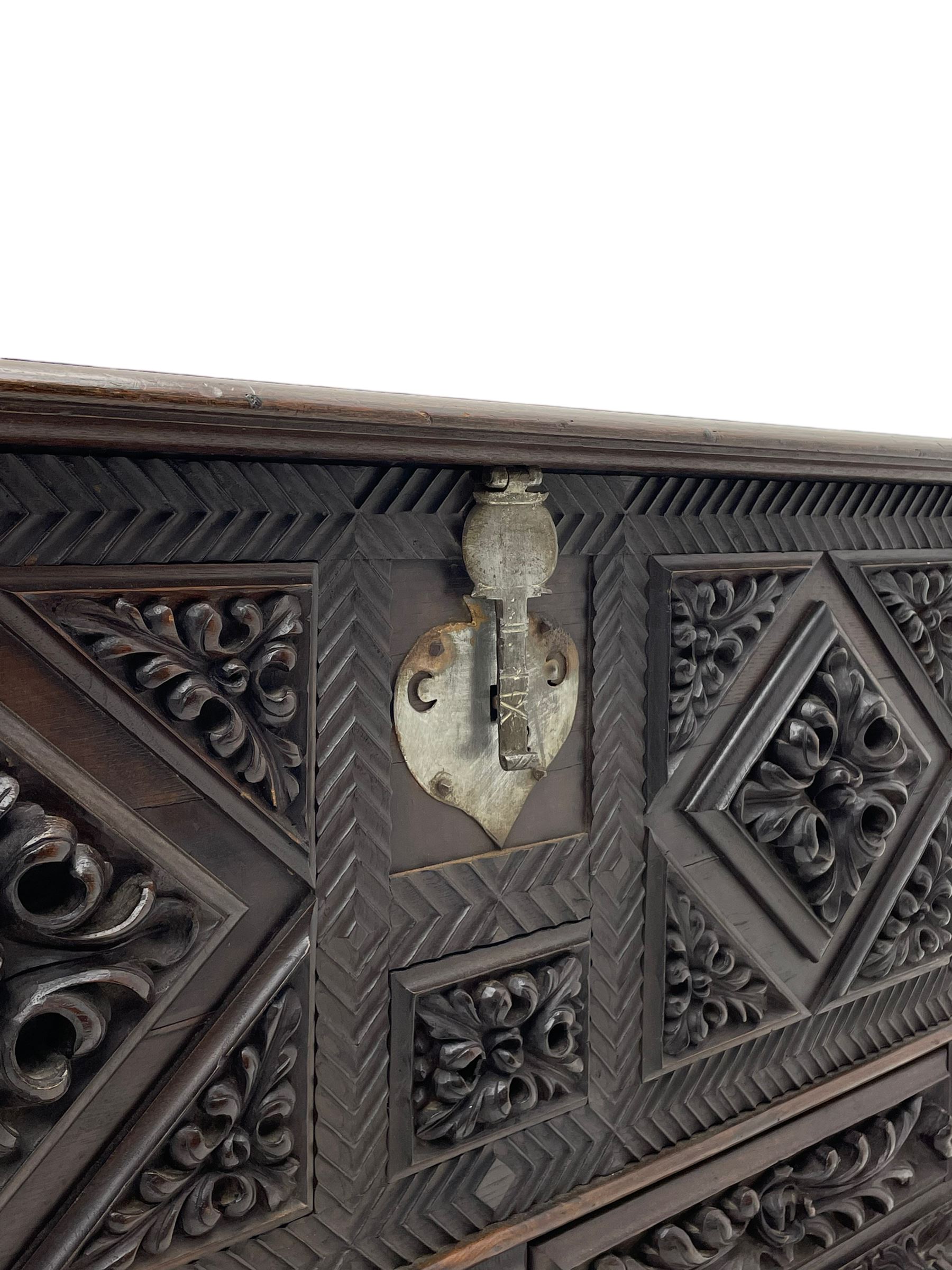Early 20th century carved hardwood kist or mule chest of small proportions, moulded rectangular hinged lid over foliage carved geometric lozenge panels, the frame carved with chevron banding, fitted with two drawers, the drawer fronts carved with extending leaf motifs over a foliage carved lower moulding, on turned feet