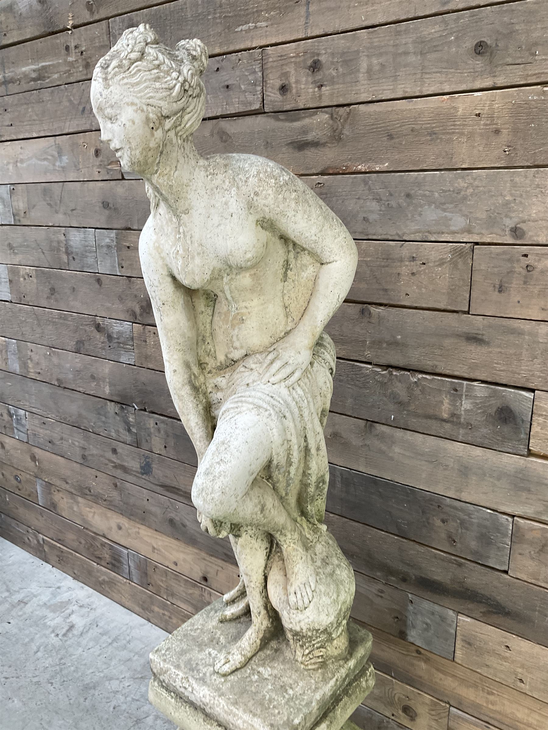 Cast stone garden statue of partially draped classical female figure on ornate pedestal 