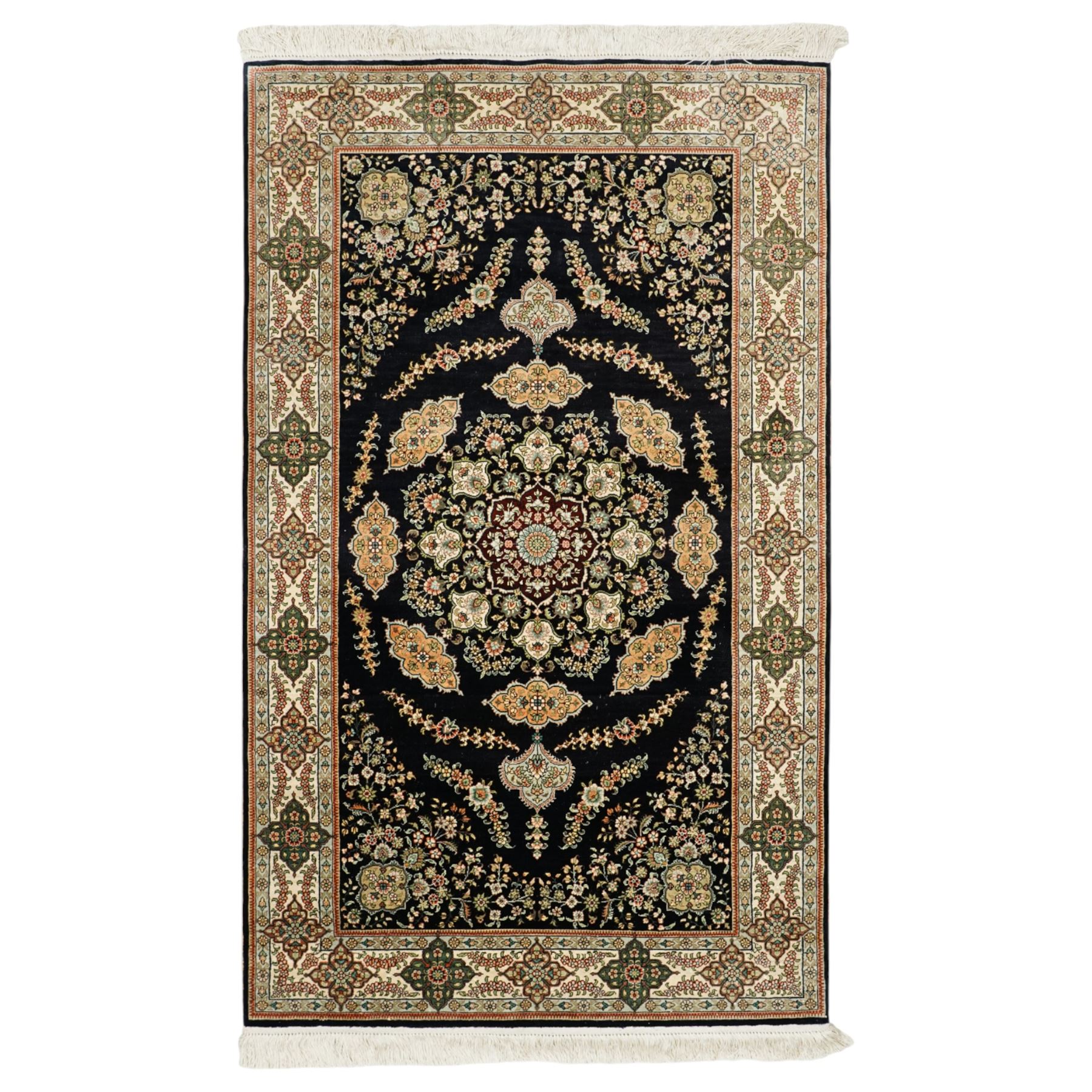 Persian-inspired Qom-style silk rug, deep indigo ground, profusely decorated with foliate motifs and a central medallion, with cotton fringe ends 