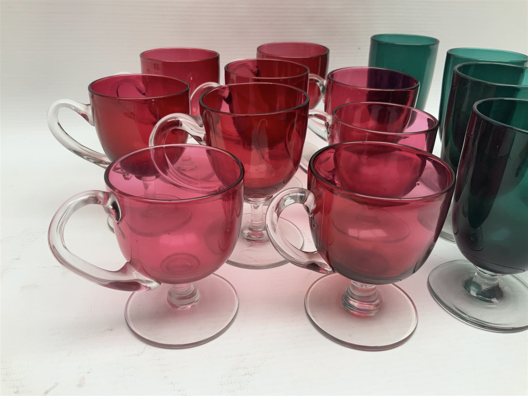 Collection of 19th century coloured glasses, to include nine cranberry glass punch cups, each with clear glass handle and foot and a set of six green glasses, with short clear stems, tallest H10cm
