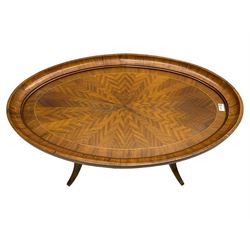 Early 20th century walnut coffee table, oval dished top with sunburst matched veneer, raised on twin cluster columns united by turned stretcher base on splayed supports