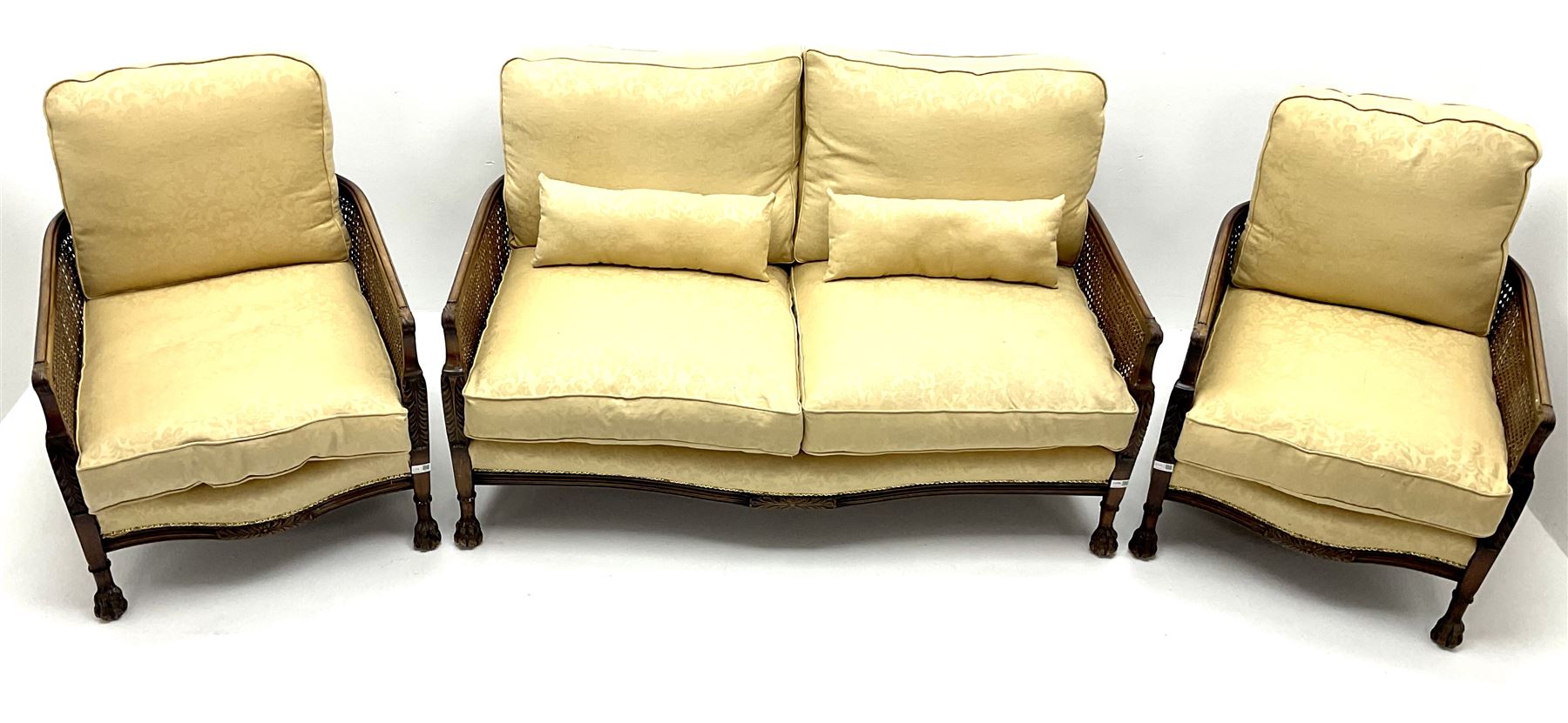 Early 20th century mahogany framed Bergere settee, double cane sides with acanthus carved arms on hairy paw feet, upholstered in a pale gold fabric (W145cm) and two matching armchairs (W66cm)