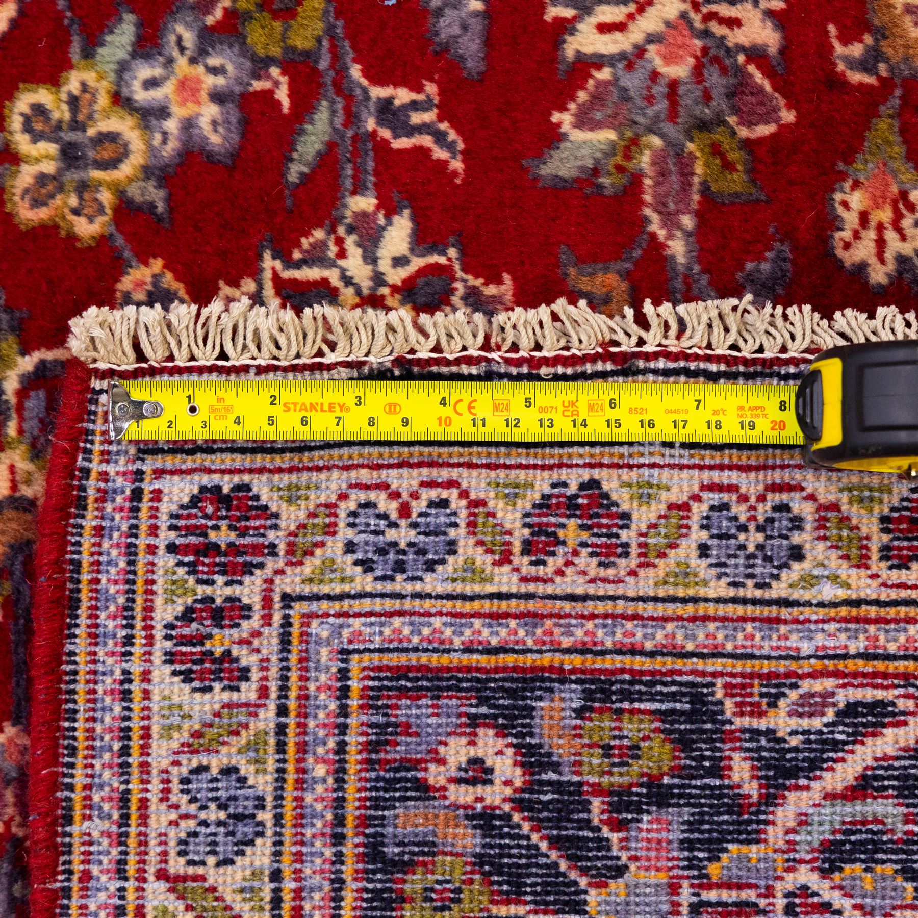 Central Persian Kashan hand-knotted rug, crimson red field with central ivory and indigo floral medallion surrounded by an all-over arrangement of finely drawn palmettes, flowering vines, and rosettes, with corresponding navy blue spandrels enclosed by a floral main border with multiple guard stripes, with cotton fringe ends    