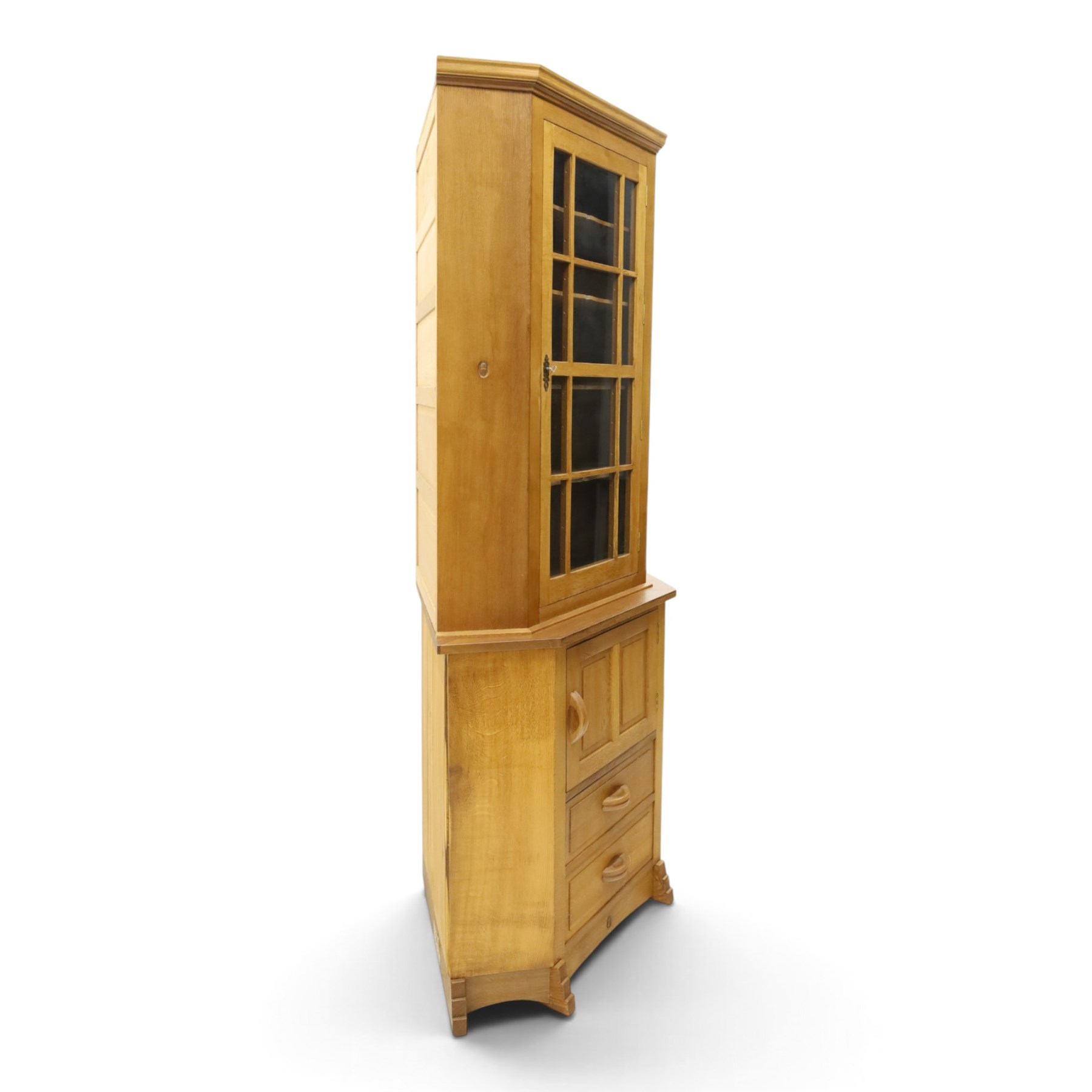 Acorn Industries - oak floor-standing corner cabinet, the top fitted with astragal glazed door enclosing four shaped shelves, the base with single panelled cupboard over two drawers, raised on four stepped feet, carved with acorn signature to top and base, by Alan Grainger, Brandsby