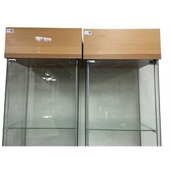 Pair light oak and glass single display cabinets, glazed back and sides with single glazed door enclosing three shelves, light fitting to top