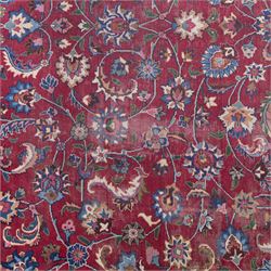 Persian Mashad design wool carpet, the red ground with dense scrolling floral and foliate decoration, within dark blue main border decorated with repeating palmettes and shaped leaves