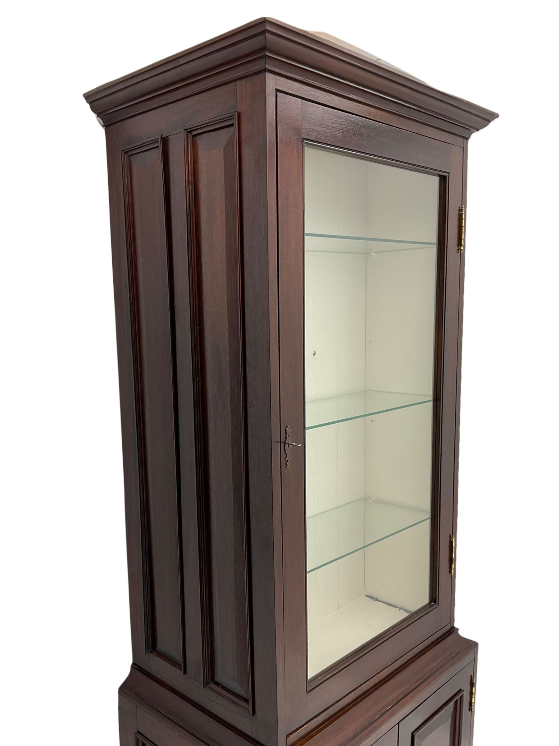 Mahogany display cabinet with hidden compartment, projecting cornice over single glazed door enclosing glass shelves, double panelled cupboard below, the interior with button releasing sliding back compartment, on bracket feet