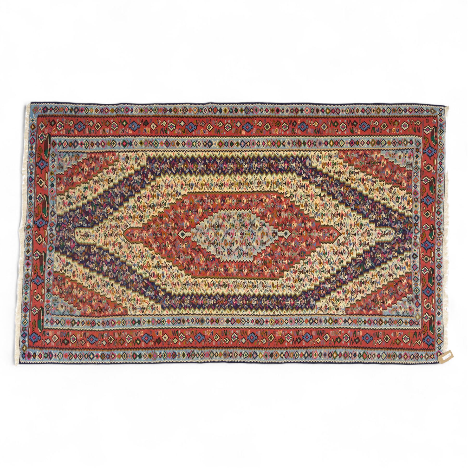 North West Persian Senneh kilim, finely woven wool with elongated central lozenge medallion on a densely patterned field of boteh motifs, in tones of red, ivory, indigo and ochre, framed by floral and diamond guard borders
