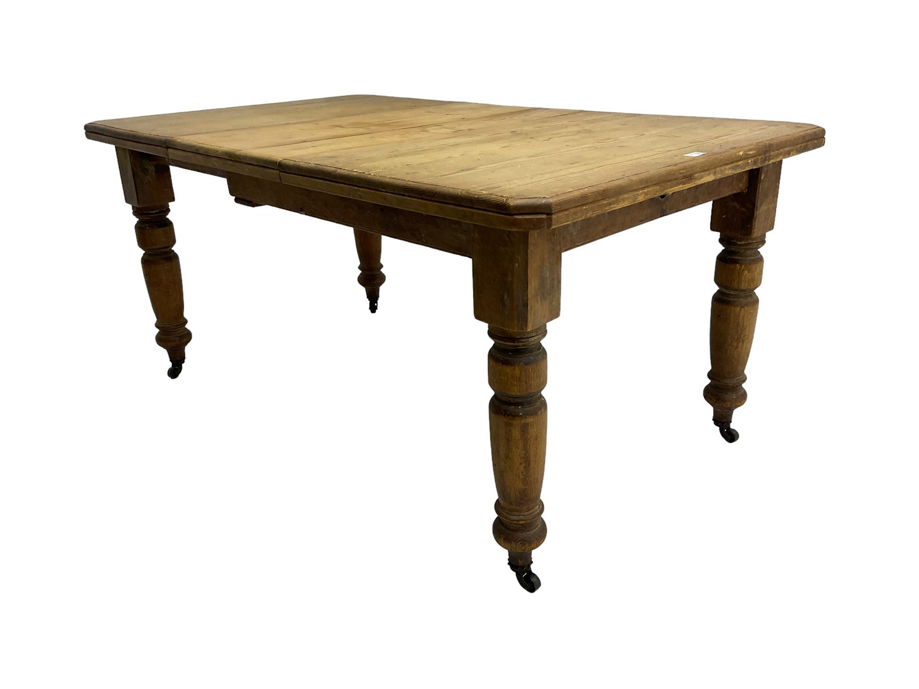 Late Victorian pine extending dining table, rectangular moulded top with canted corners and additional leaf, on turned supports with brass castors 