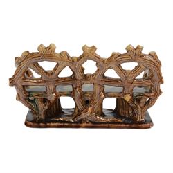 19th century pottery model of a bench, possibly Skey Pottery Tamworth, Staffordshire, the shaped seat mottled in shades of green, dark blue, yellow and brown, supported upon naturalistically modelled tree stumps, the arms and back modelled as intertwined branches, H14cm W21cm D10cm