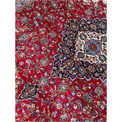 Persian Kashan crimson ground carpet, floral pattern indigo ground central medallion and matching spandrels, the field decorated densely with scrolling foliate patterns and floral motifs, the main border decorated with scrolling branches and palmettes, within floral pattern guard stripes