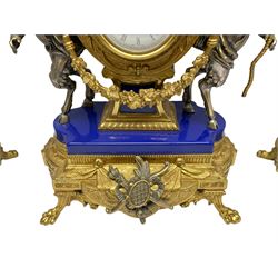 A 20th century continental gilt metal Lyre mantle clock with a pair of matching six light candelabra, spring driven movement housed in a gilt drum case on a brass and cobalt blue base with paw feet, two bronzed metal figures of mythological cherubs with animal legs and cloven hooves supporting a festooned garland swag, eight-day twin barrel striking movement with a floating lever balance escapement, striking the hours and half-hours on two bells, white enamel dial with roman numerals, minute track and pierced steel hands, dial inscribed “Imperial”. 